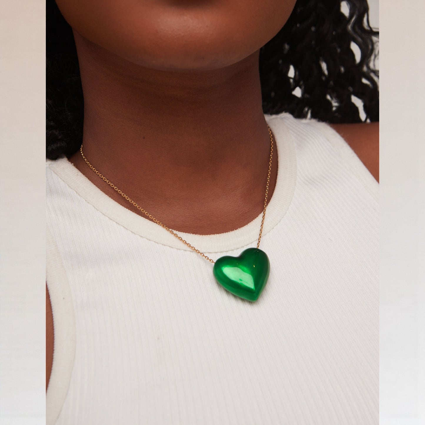Person wearing a gold necklace with a green heart-shaped pendant