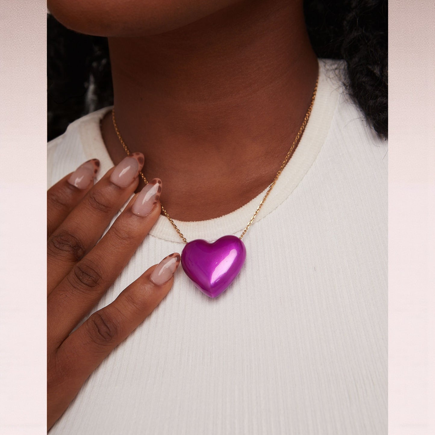 Purple heart-shaped pendant on a gold chain worn by a person.