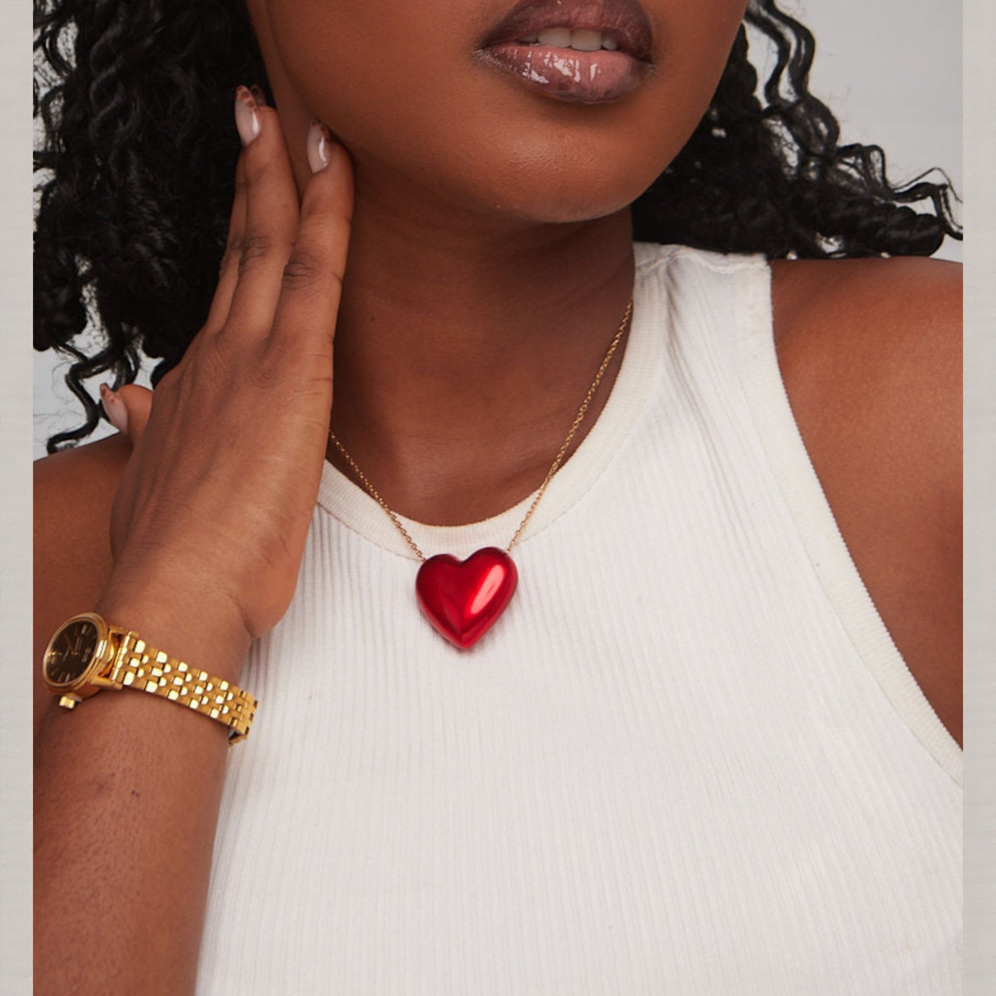 Woman wearing a gold watch and red heart necklace against a neutral background