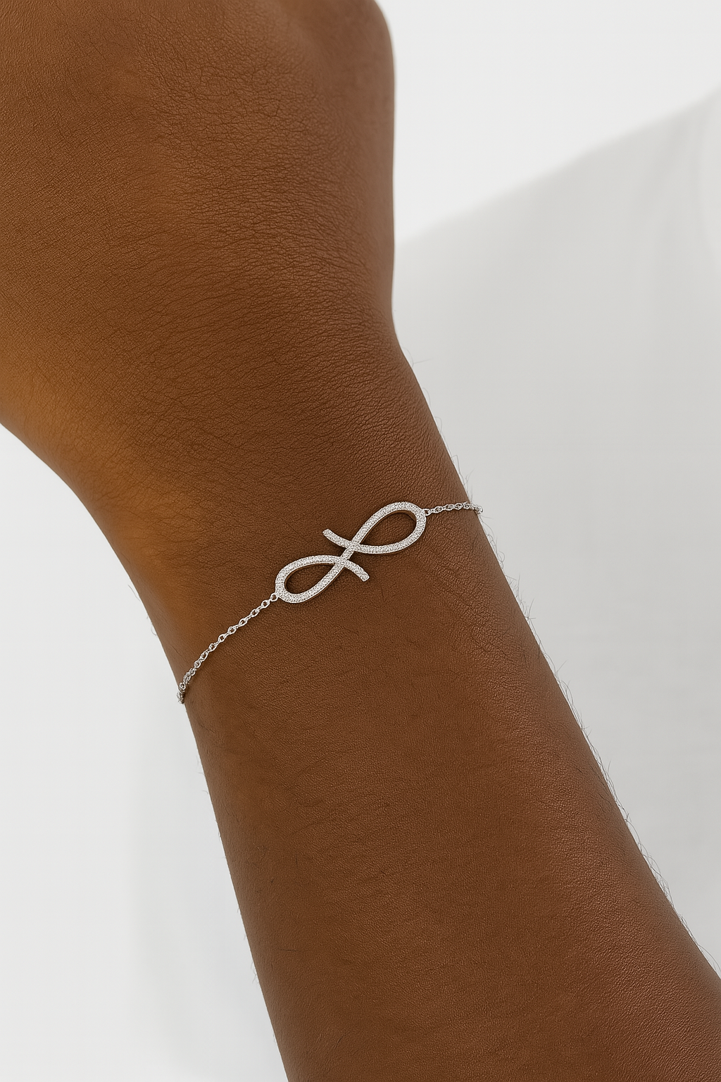 Silver infinity bracelet on a wrist with a plain background