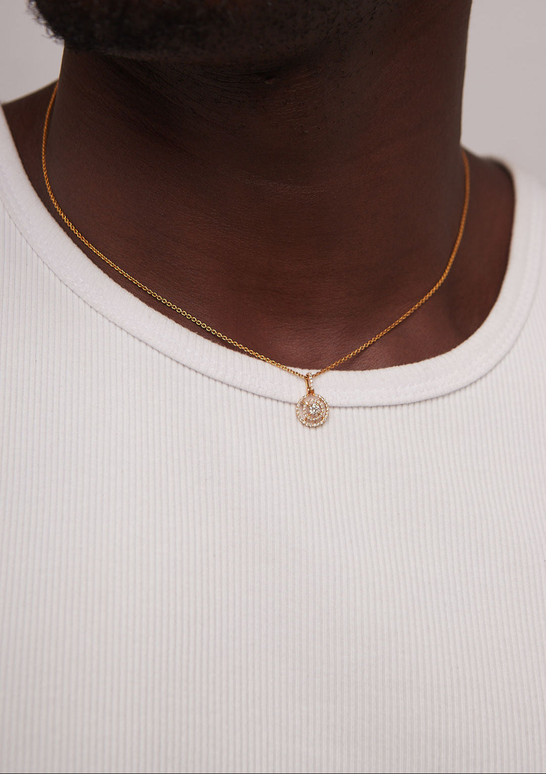Gold necklace with a pendant worn by a person on a plain background