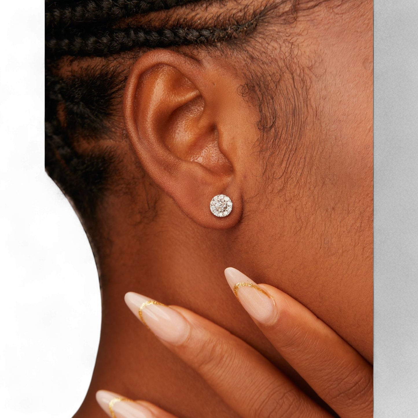 Close-up of an ear wearing a diamond earring with a hand touching the cheek.