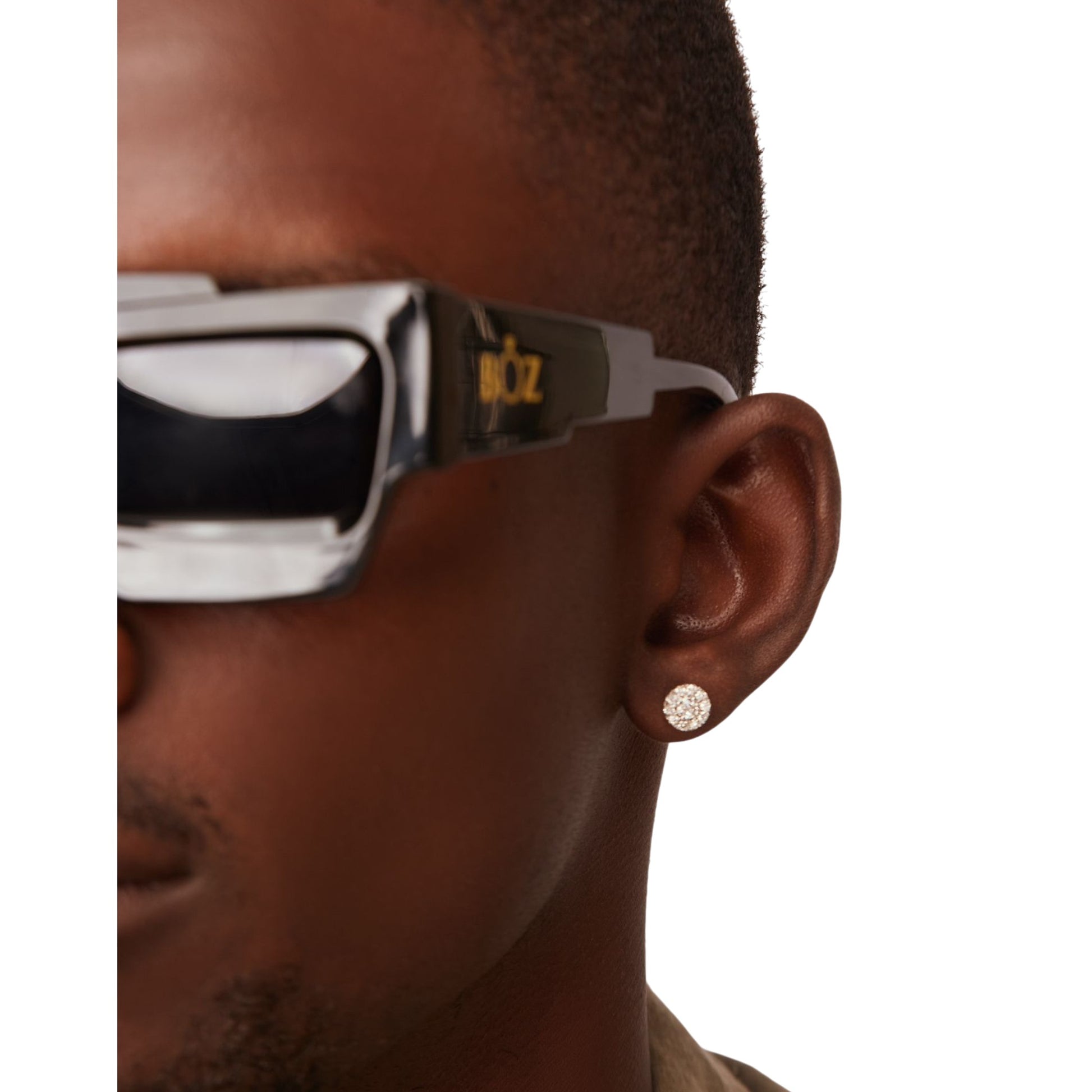 Close-up of a person wearing sunglasses with a brand logo and a diamond earring.