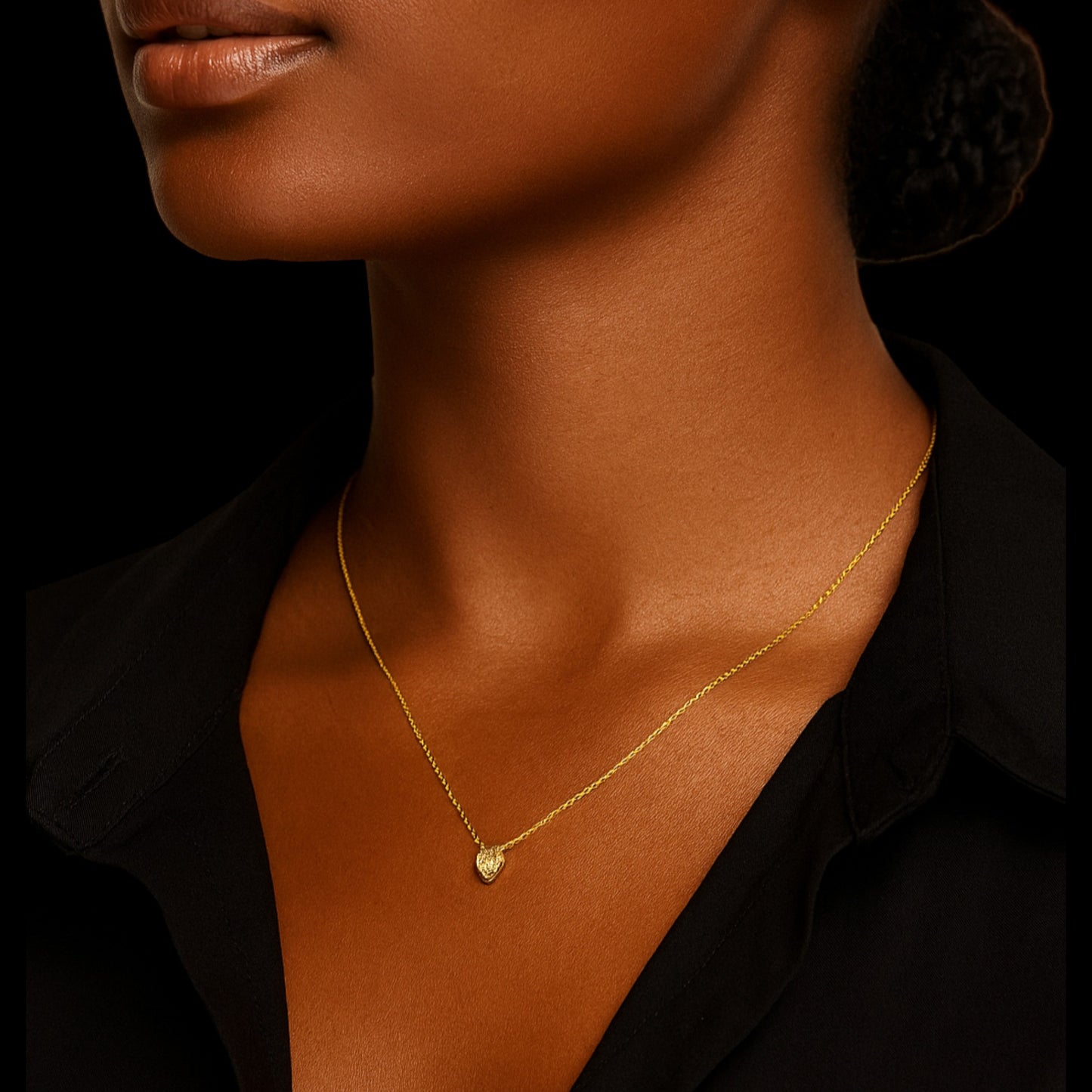 Close-up of a person wearing a gold necklace with a heart pendant against a black background