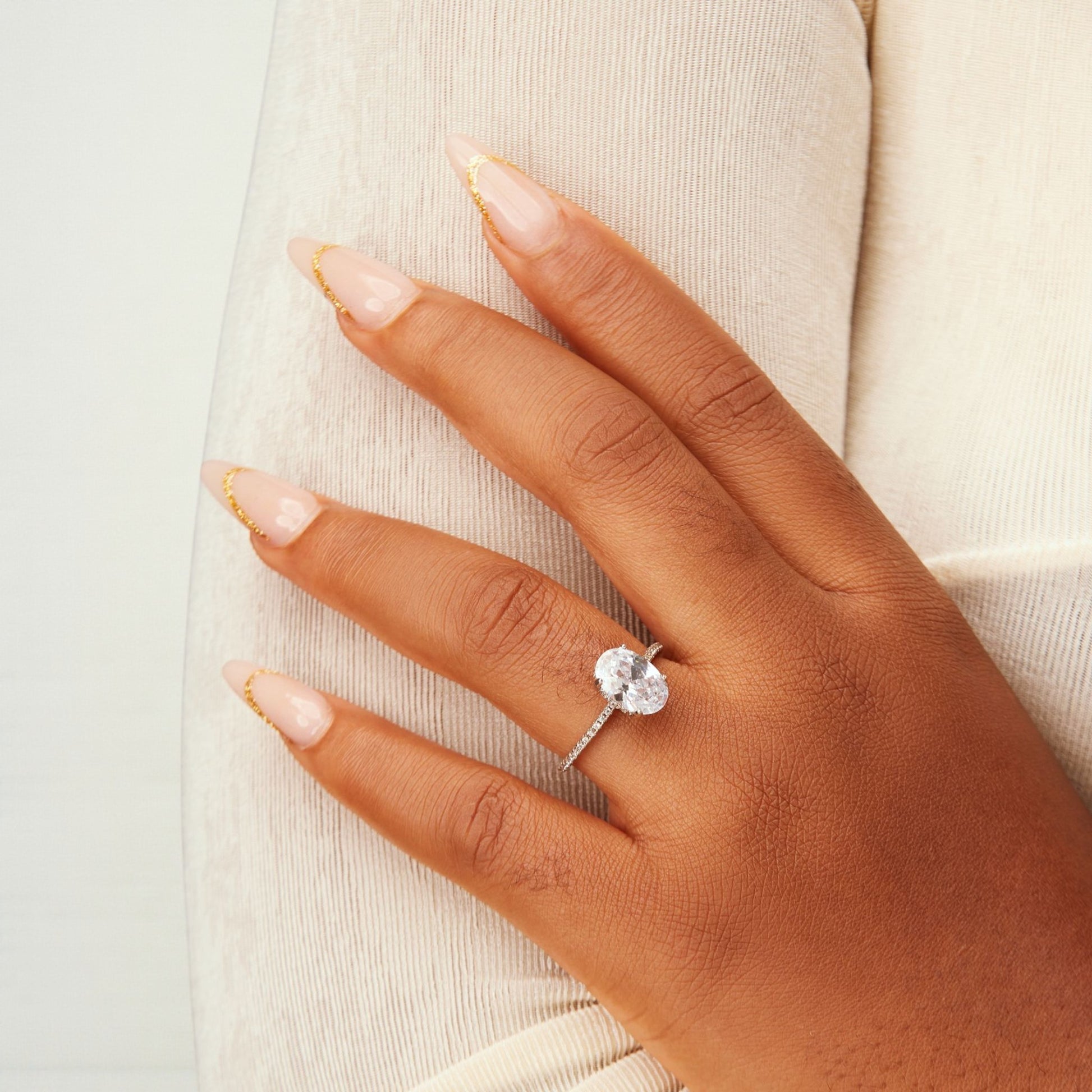 Hand wearing a diamond ring on a neutral background