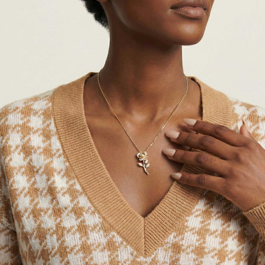 Woman wearing a gold necklace with a rose pendant, wearing a patterned sweater.