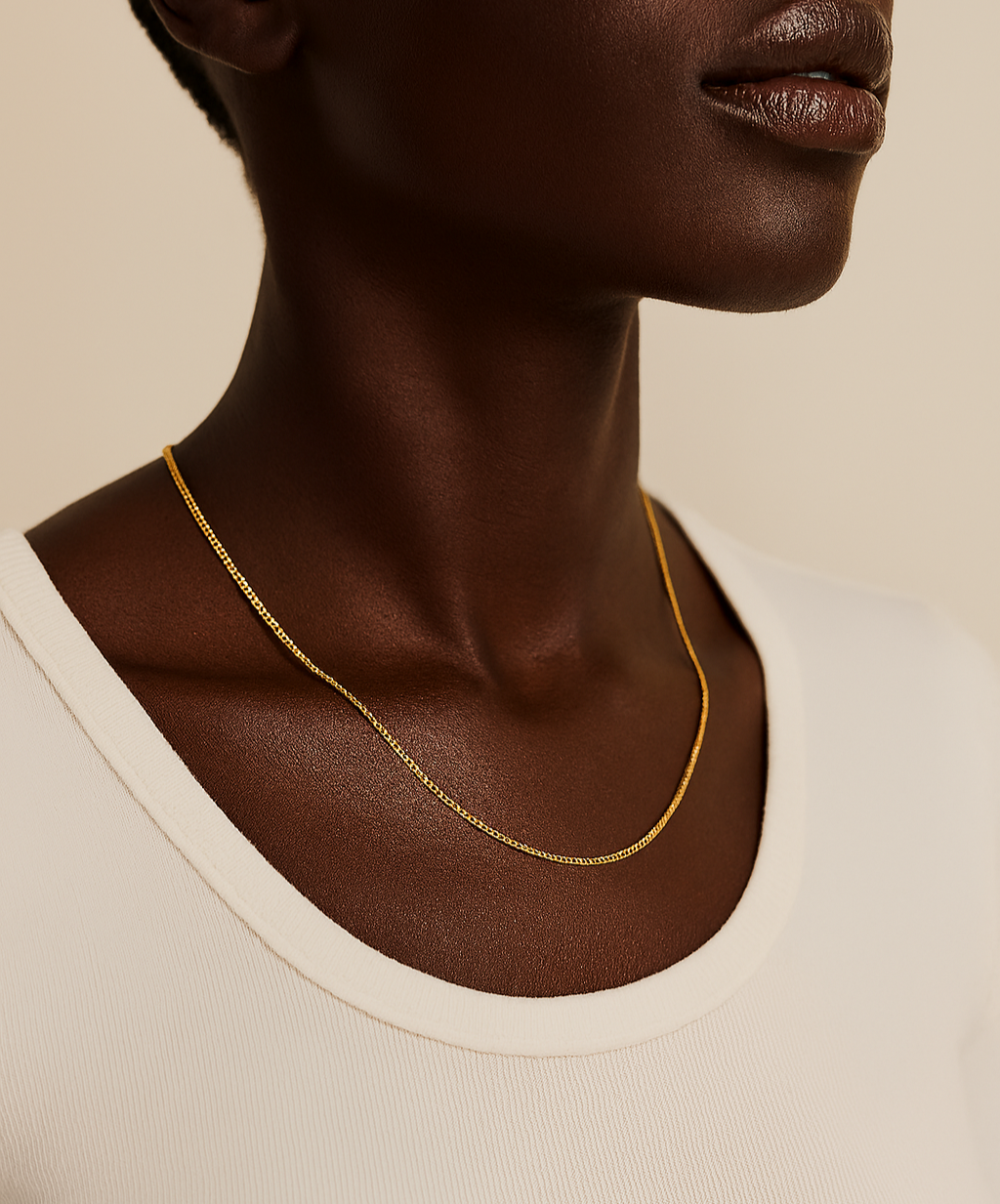 Close-up of a person wearing a gold necklace against a neutral background