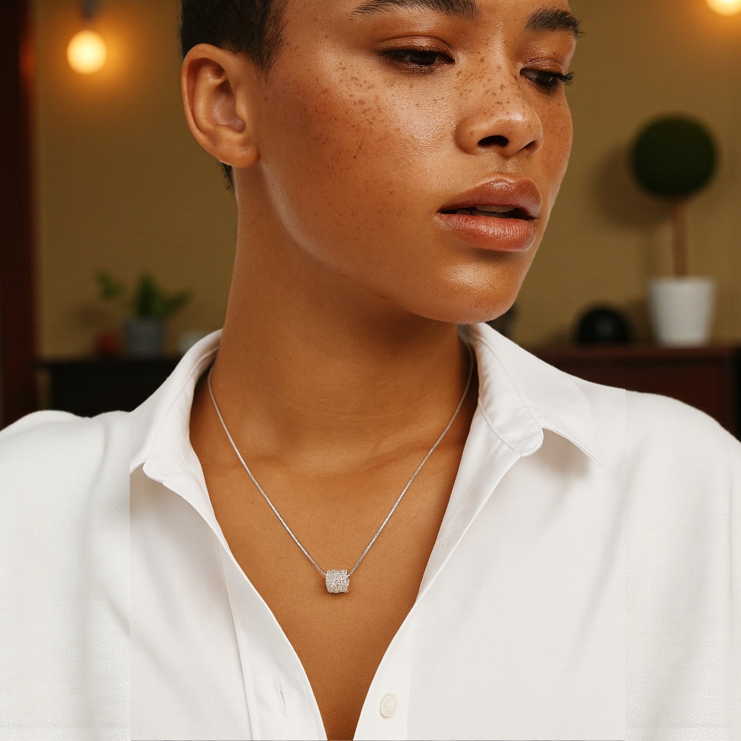 Woman wearing a silver necklace with a diamond pendant in a softly lit room.