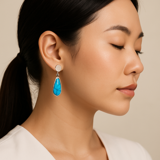 Close-up of a woman wearing a turquoise teardrop earring against a neutral background