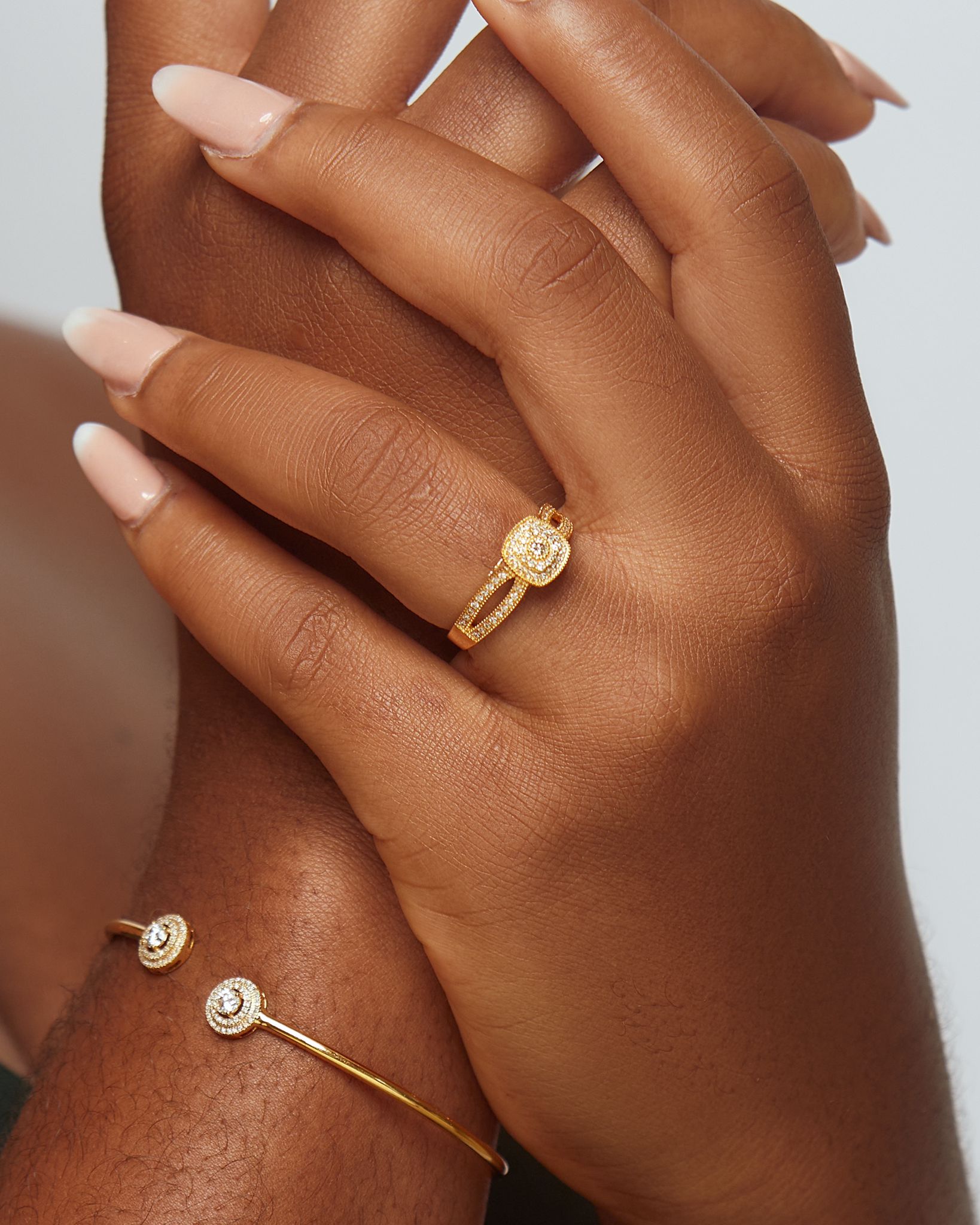 Close-up of a hand wearing a gold ring and bracelet on a neutral background