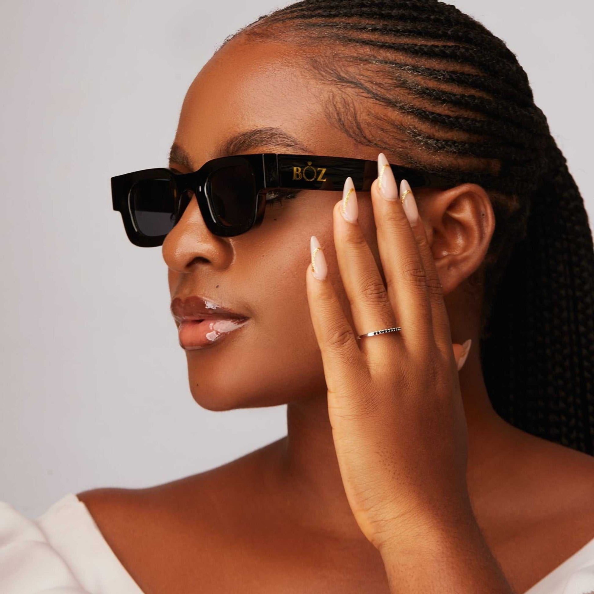 Woman wearing sunglasses with a brand logo, holding hand to face
