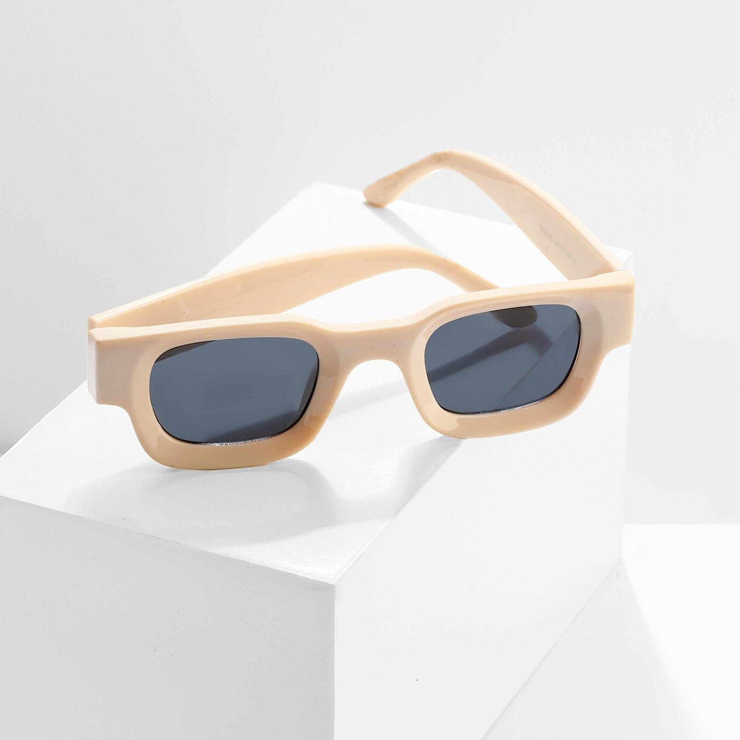 Beige sunglasses with dark lenses on a light gray background