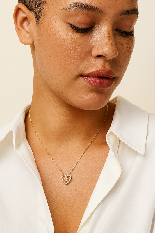 Close-up of a person wearing a gold necklace with a heart pendant on a neutral background