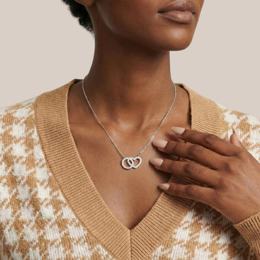 Woman wearing a silver necklace with interlocking heart pendants, wearing a beige sweater.