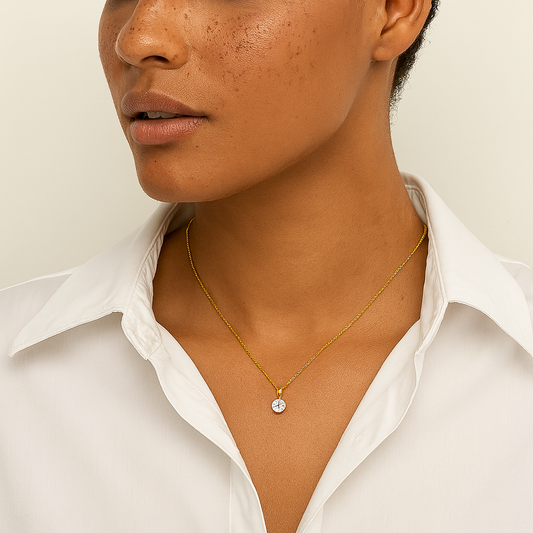 Woman wearing a gold necklace with a small round pendant against a neutral background