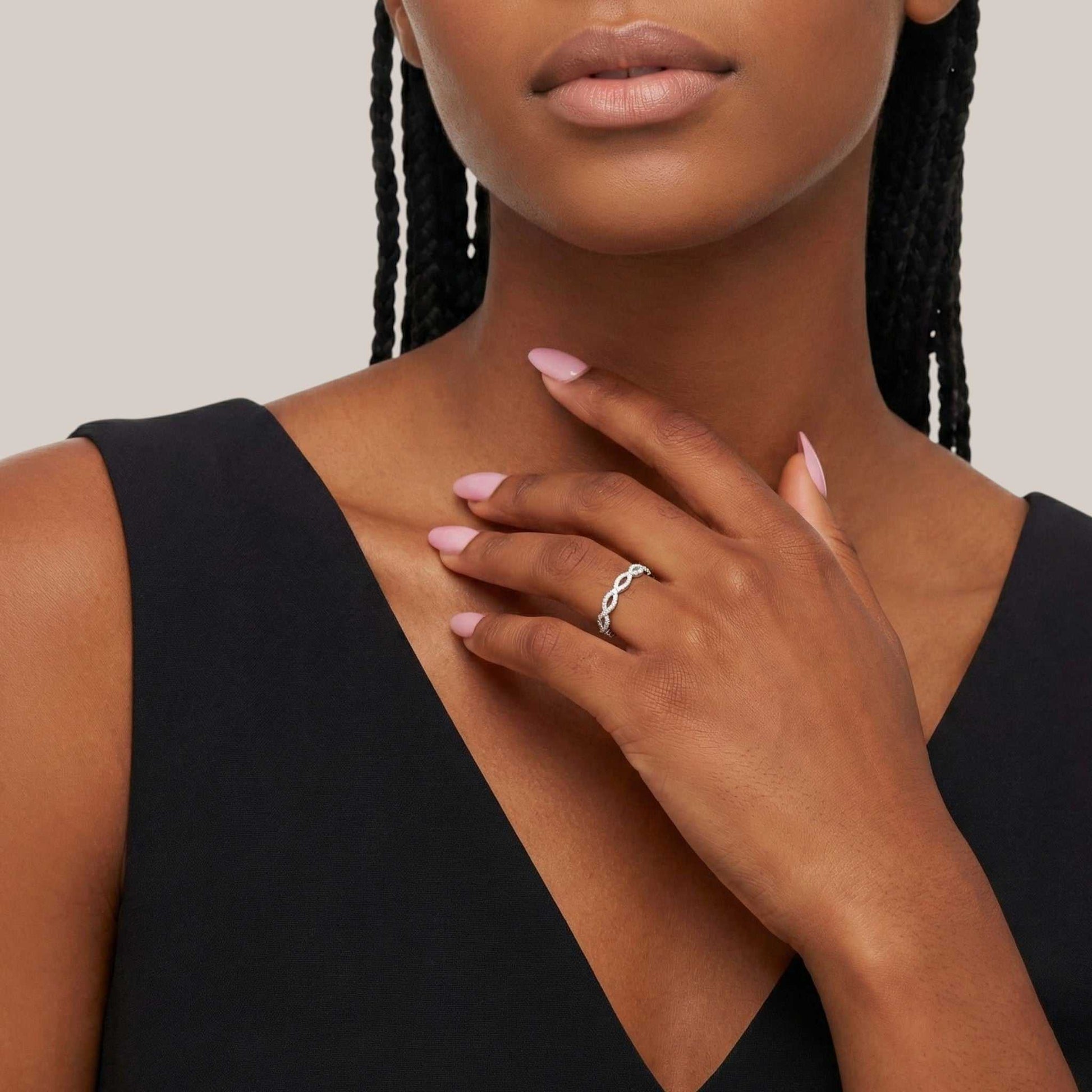Woman wearing a black dress with a ring on her finger, against a neutral background