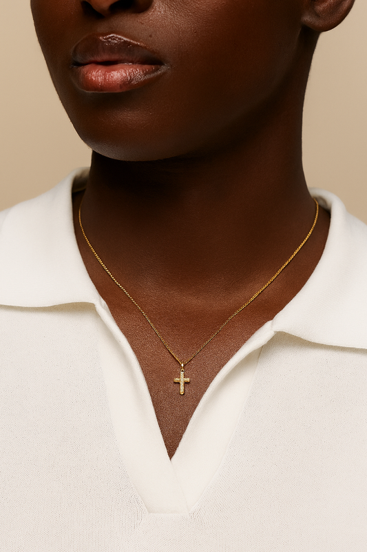 Close-up of a person wearing a gold necklace with a cross pendant on a beige background