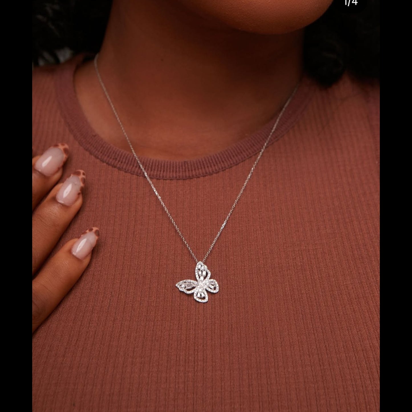 Silver butterfly necklace on a person wearing a brown top