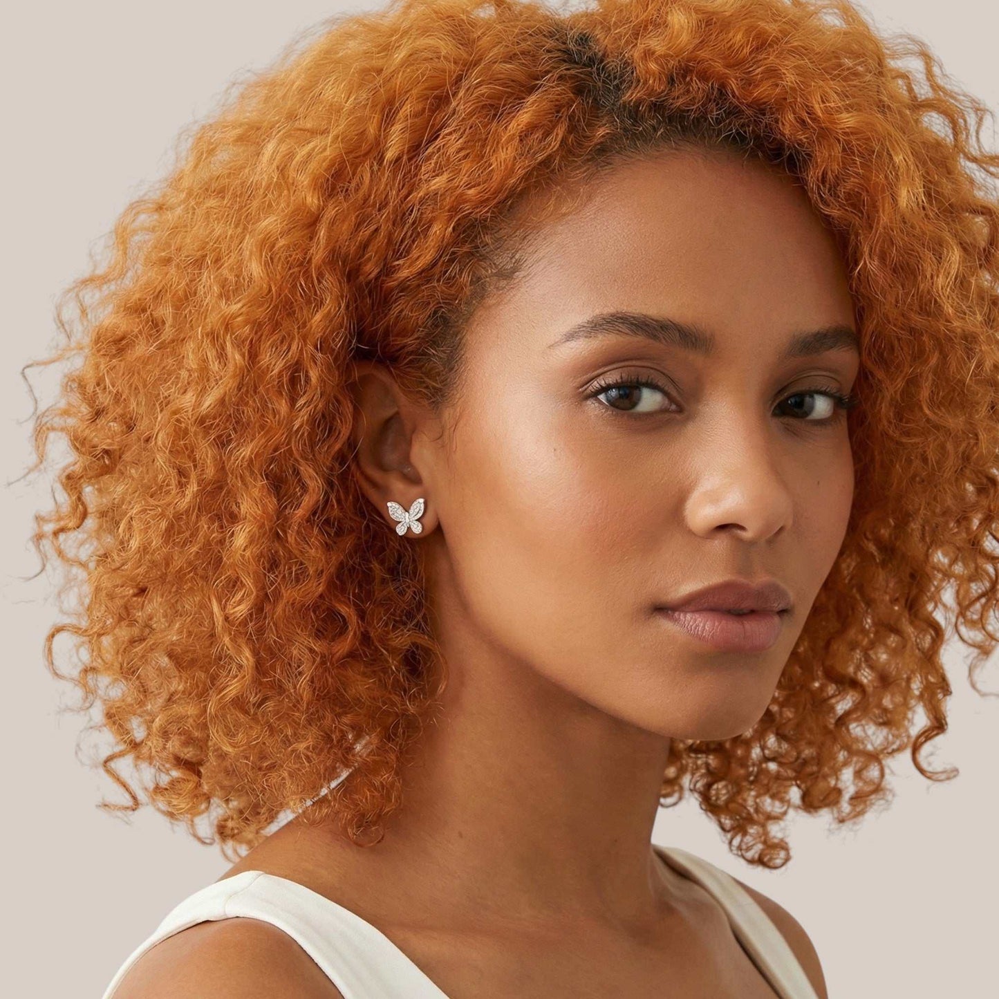 Woman with curly orange hair wearing a butterfly earring on a light background