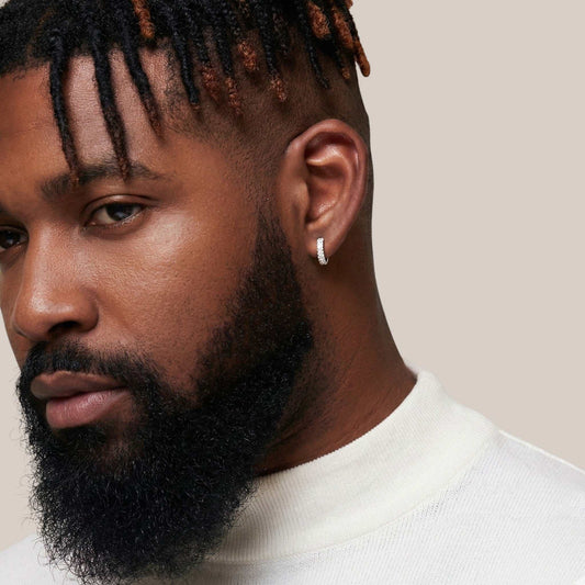 Man with styled hair and beard wearing a white turtleneck against a neutral background