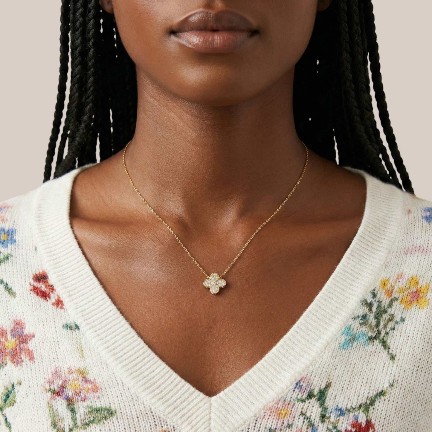 Woman wearing a gold necklace with a clover pendant against a neutral background