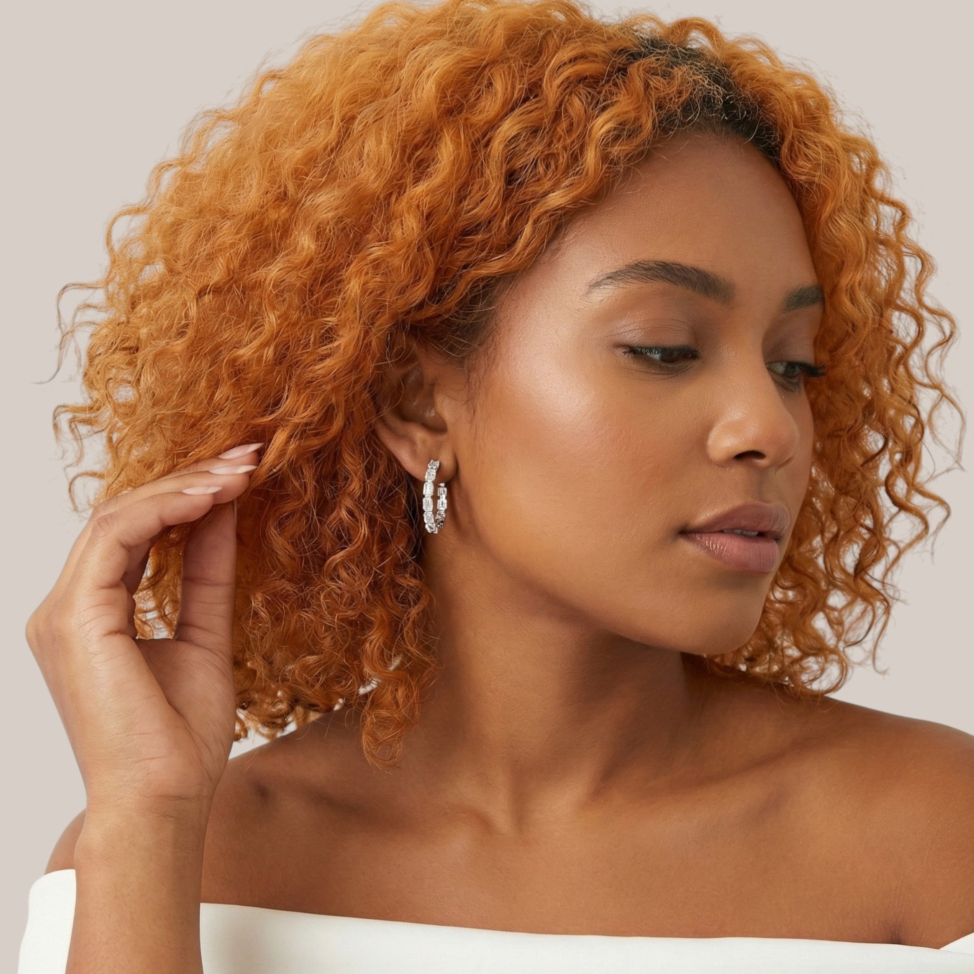 Woman with styled hair and earrings against a neutral background