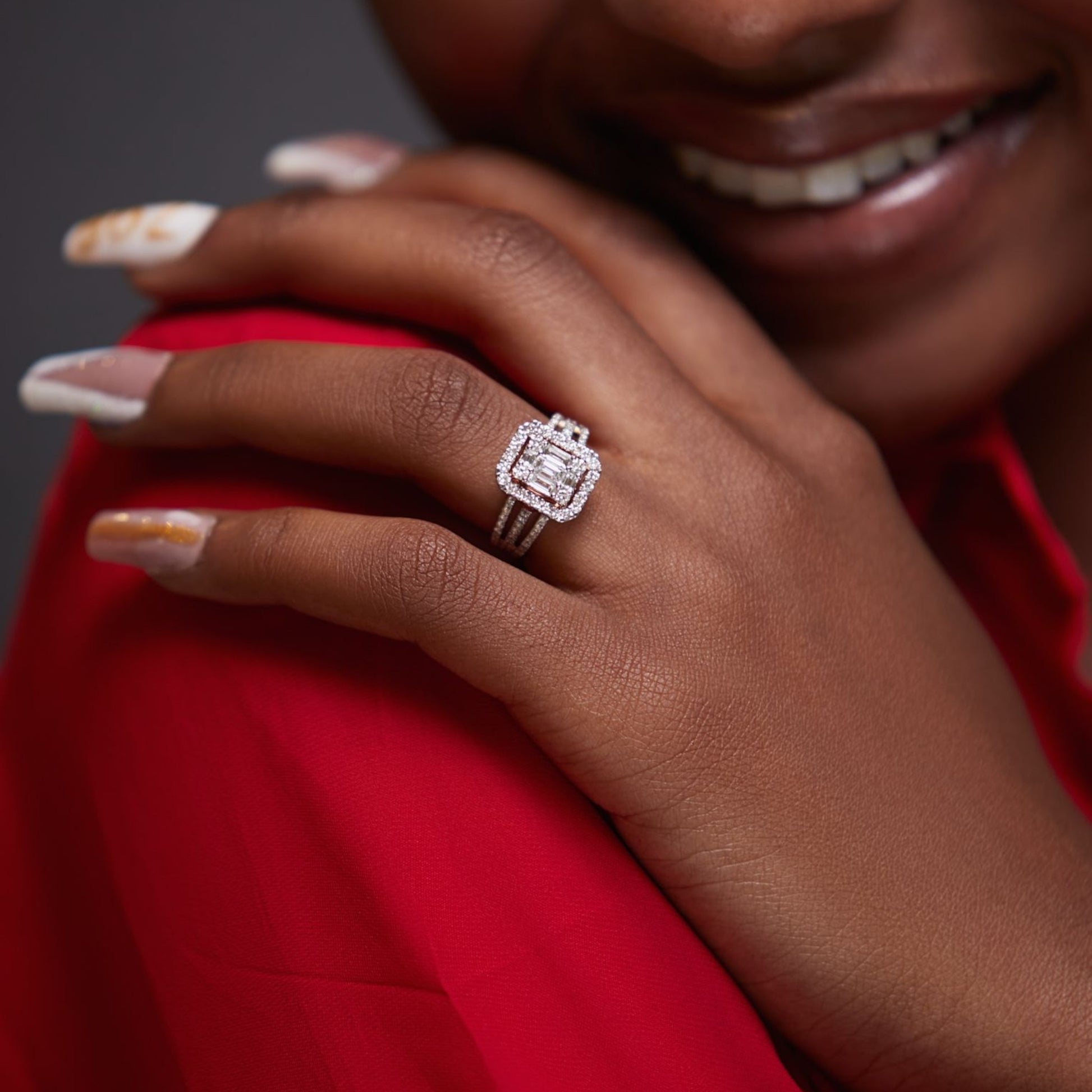 Close-up of a hand wearing a diamond ring with a red garment in the background