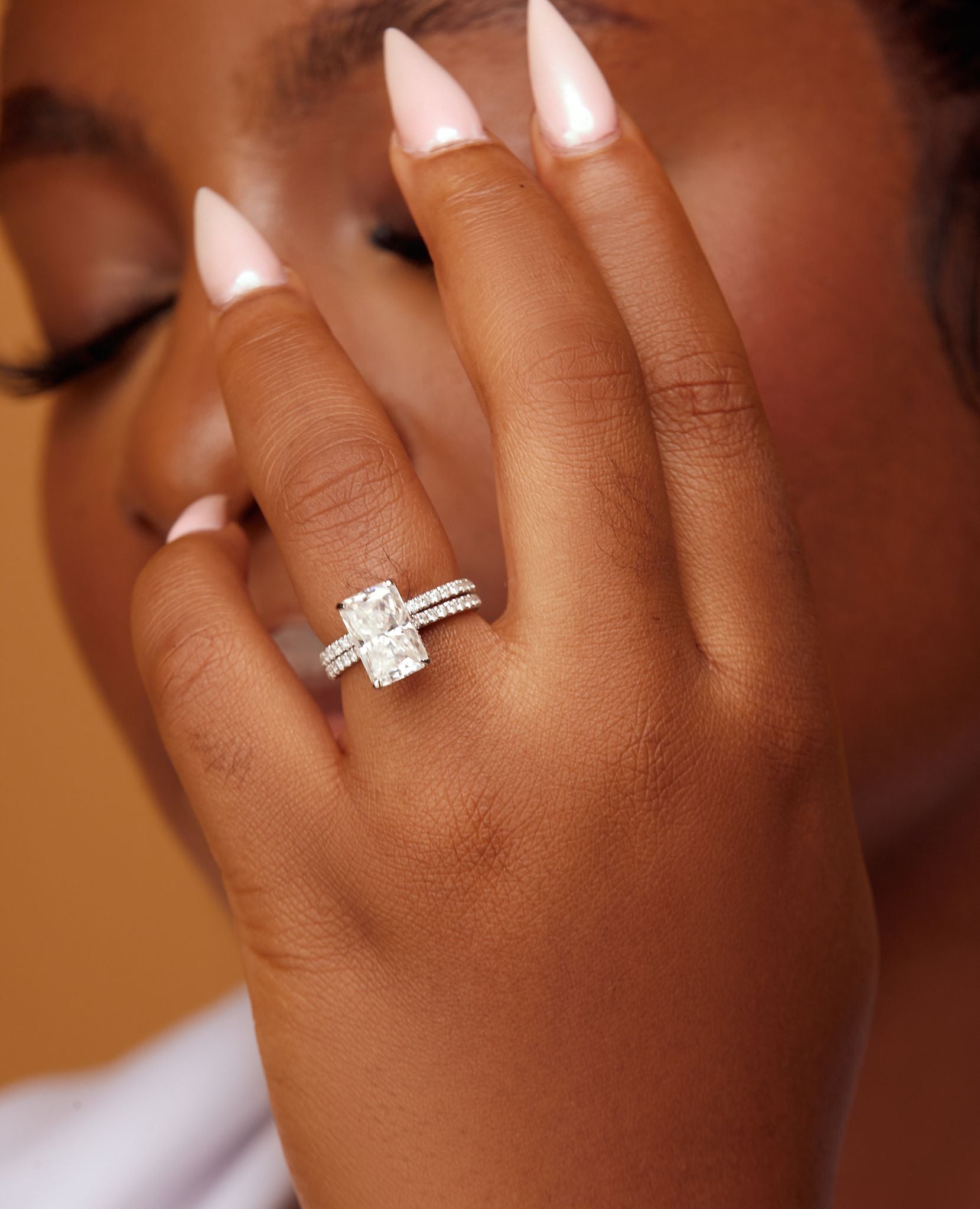A person's hand holding a radiant cut engagement ring with moissanite and natural diamonds, set in 18 karat gold.