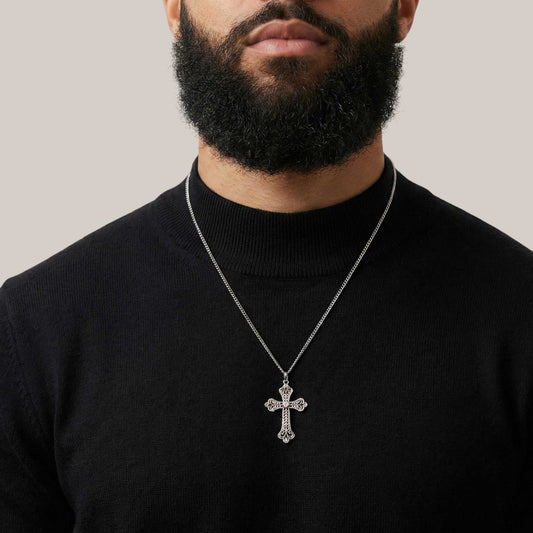 Man wearing a black turtleneck with a silver cross necklace against a neutral background