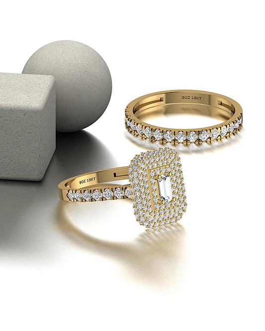 Two 18 karat gold rings, one with a baguette cut diamond centerpiece and surrounding smaller diamonds, and another with a square cut diamond centerpiece. Rings are displayed on a reflective surface with a grey background.