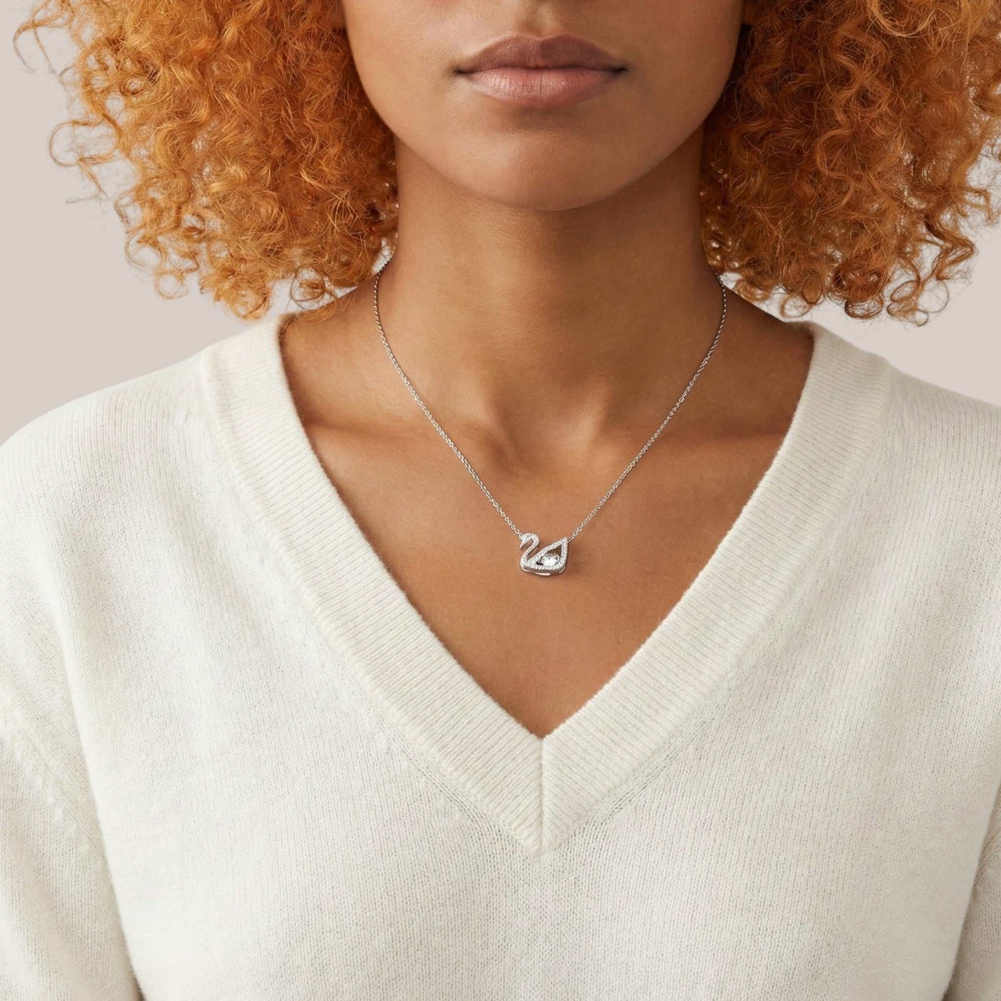 Person wearing a silver necklace with a heart pendant on a neutral background