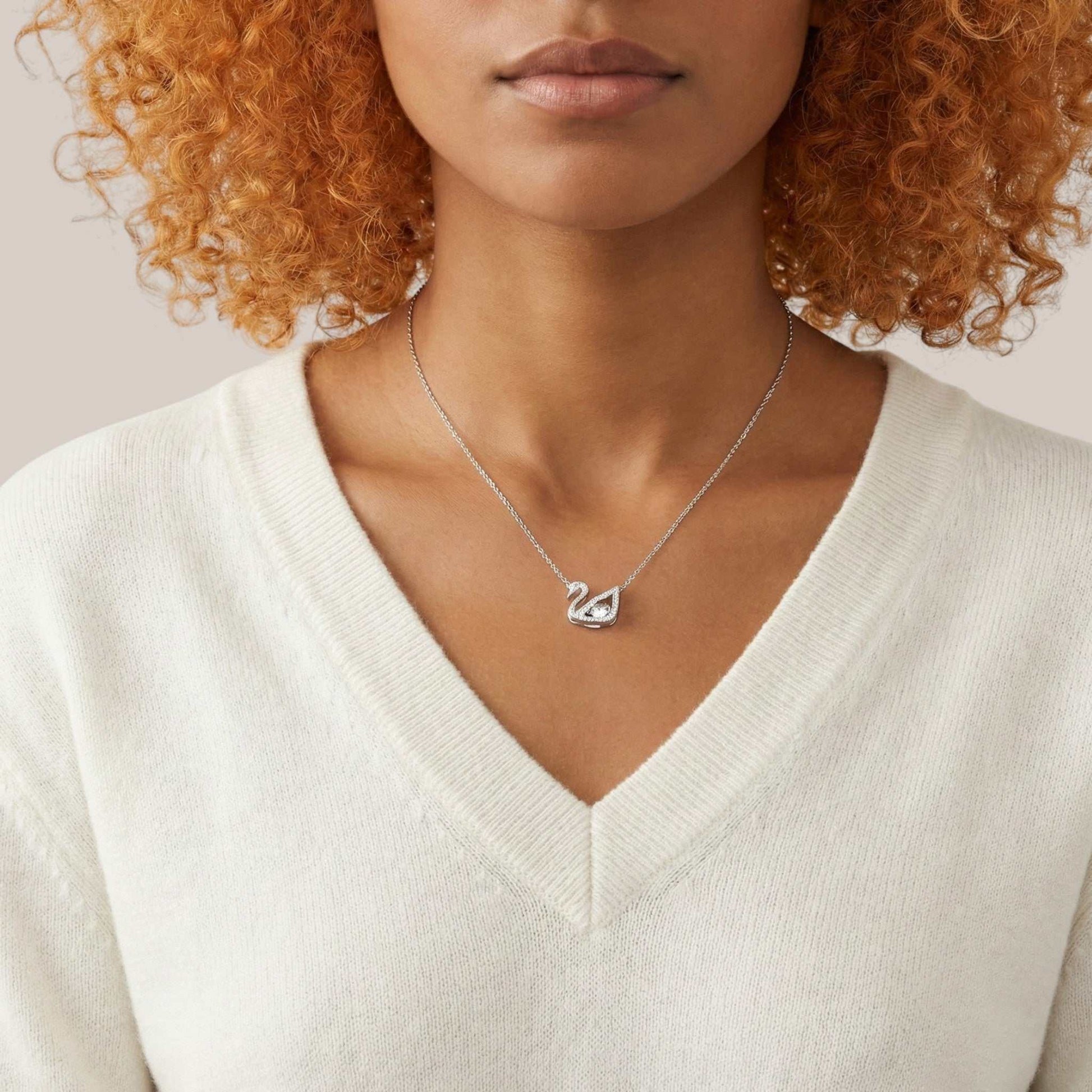 Person wearing a silver necklace with a heart pendant on a neutral background