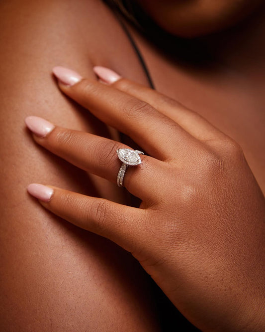A close-up of a person's hand showcasing a marquise cut moissanite and diamond bridal set ring on the finger.