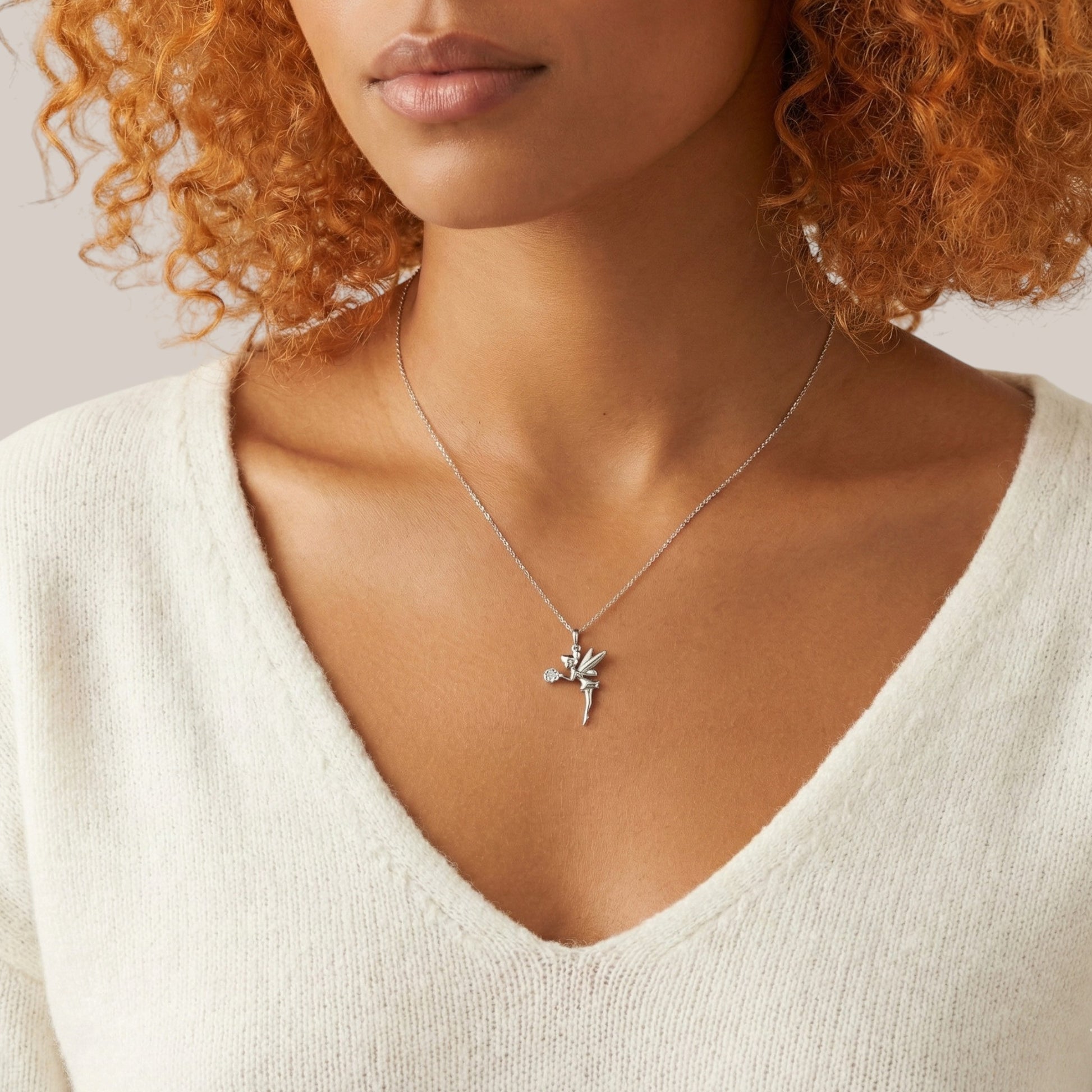 Woman wearing a silver fairy pendant necklace against a neutral background