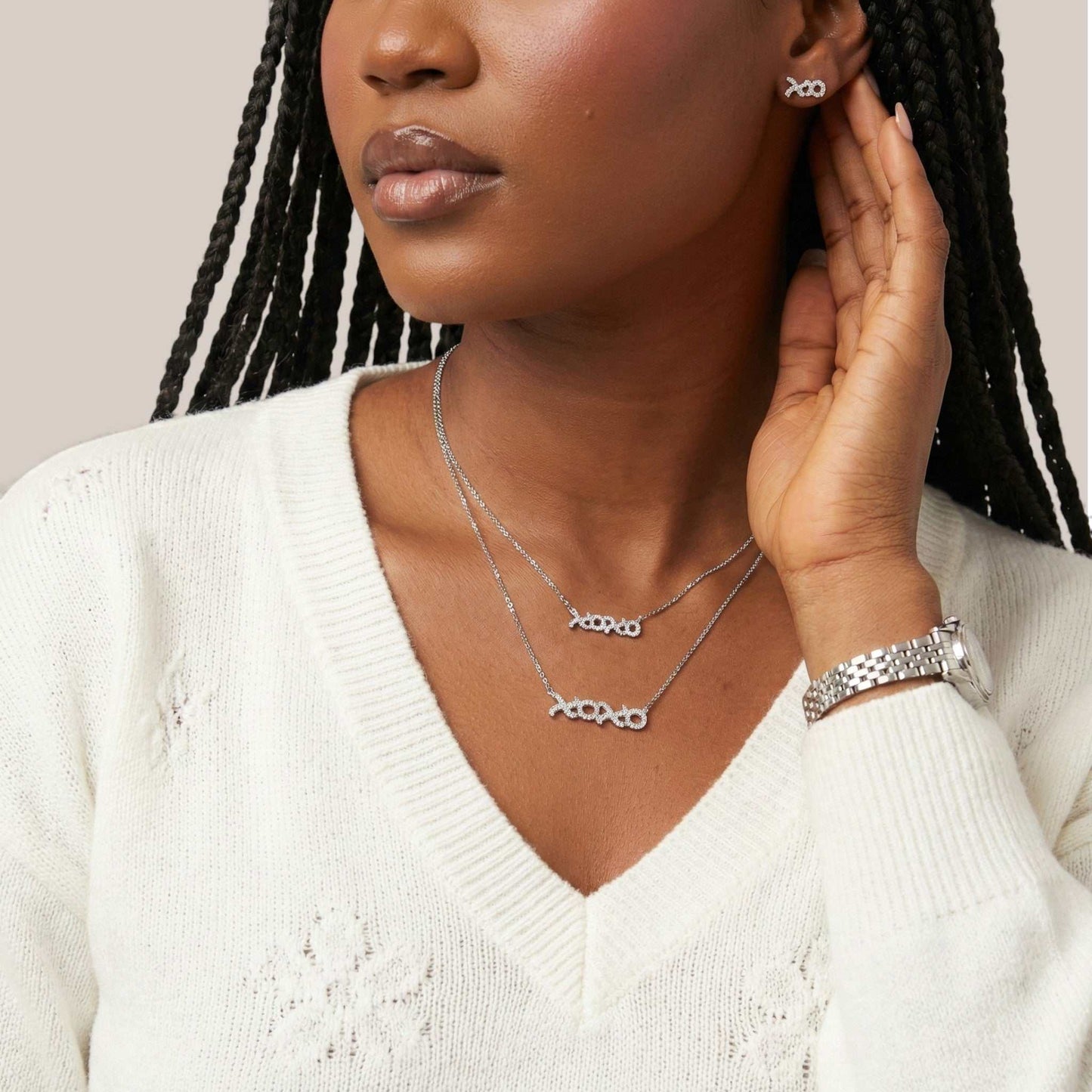 Woman wearing silver jewelry including necklaces, earrings, and bracelet on a neutral background
