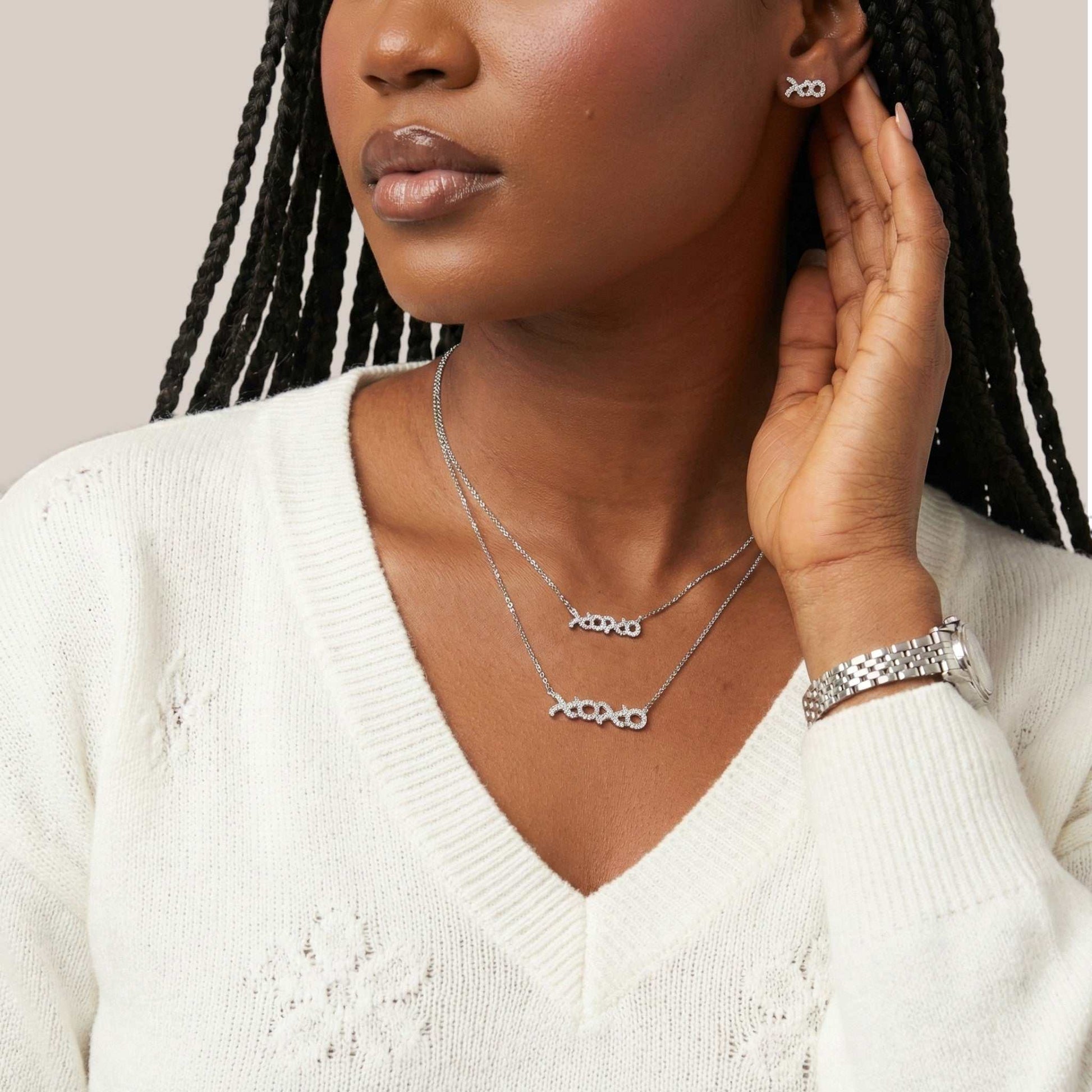 Woman wearing silver jewelry including necklaces, earrings, and bracelet on a neutral background
