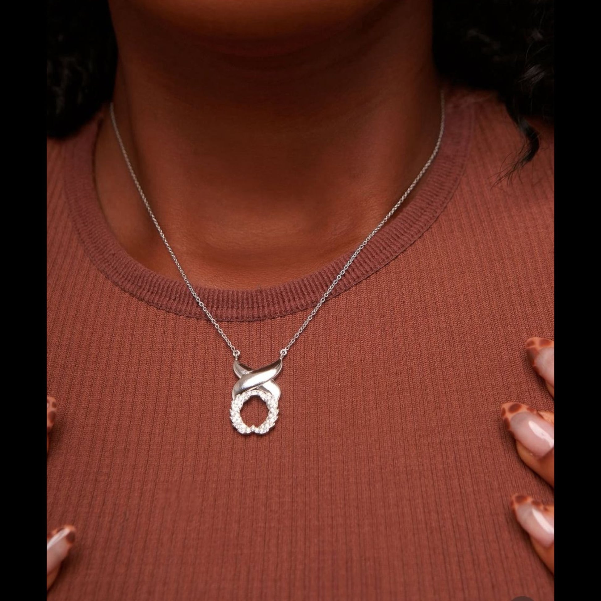 Silver necklace with a pendant on a person wearing a brown top.