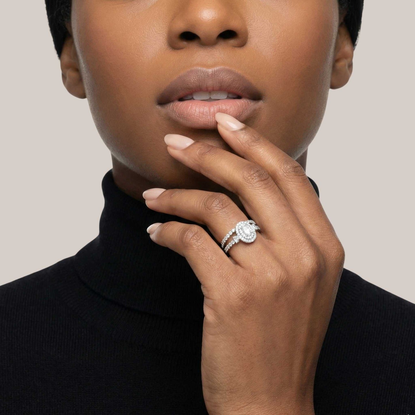 Close-up of a person wearing a diamond ring on a neutral background